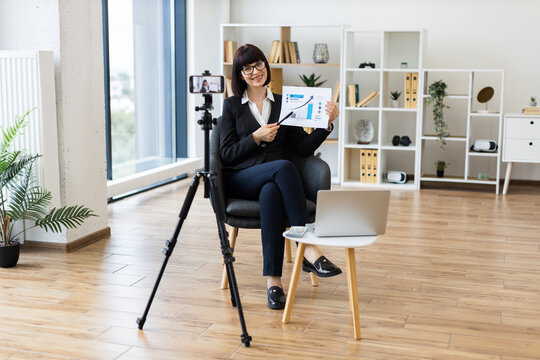 Caucasian woman, business professional, presenting growth graphs during vlog in modern office setup.
