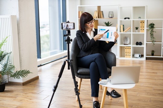 Caucasian woman presenting business analytics on camera through blogging using report and statistics chart.