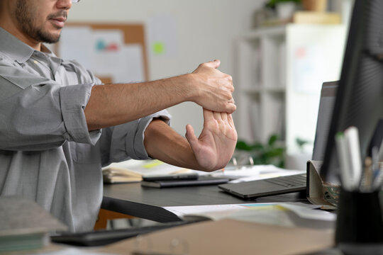 Fototapeta Businessman suffering from wrist pain while working on computer, Businessman massaging his hand and wrist after long hours in front of a computer