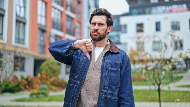 Man expresses strong disapproval with firm thumbs-down gesture, conveying dissatisfaction and negative opinion. Visual highlights feeling of unhappiness or rejection regarding choice, evaluation.