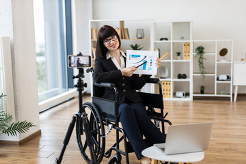 Caucasian woman in professional office showing financial chart during remote video blogging session.