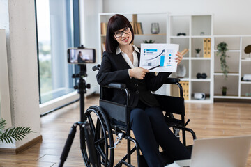 Caucasian woman in professional office showing financial chart during remote video blogging session.