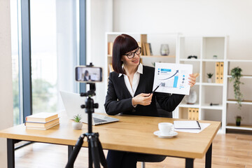 Caucasian woman sitting at table recording blog video about business performance statistics and growth analytics.