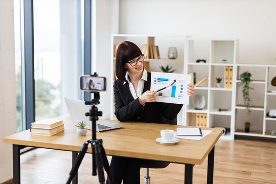 Caucasian woman sitting at table recording blog video about business performance statistics and growth analytics.