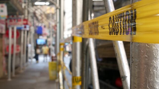 Caution yellow tape and scaffolding on pavement under construction in Manhattan, New York City, United States. Renovation or maintenance, strip barricade or barrier ribbon, scaffold safety warning.