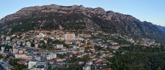 Twilight aerial panorama of Krujë city with the Moon rising above the mountain ridge and fortress under soft evening light.