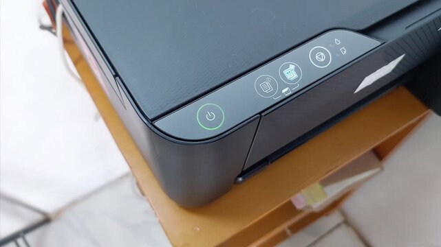 Close-up of Finger Pressing the Power Button on a Black Printer or Scanner