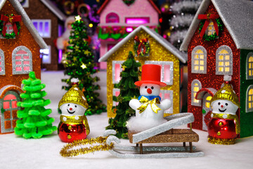 Among the houses of the Christmas town there are two snowmen and one snowman in a red hat on a sled between them
