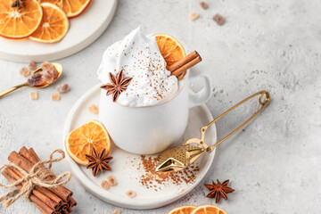 Hot cocoa drink with whipped cream, dried orange and spices in mug on white festive christmas table background