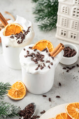 Hot chocolate drink with whipped cream, dried orange and spices in mug on white festive christmas table background