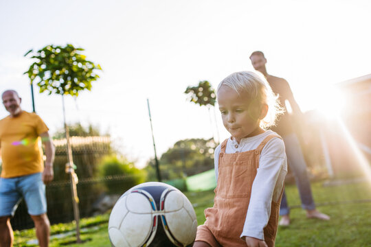 Little boy playing football with father and grandfather in backyard.