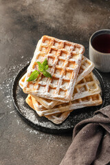 Delicious belgian waffles in stack with powdered sugar on a plate on dark background with copy space