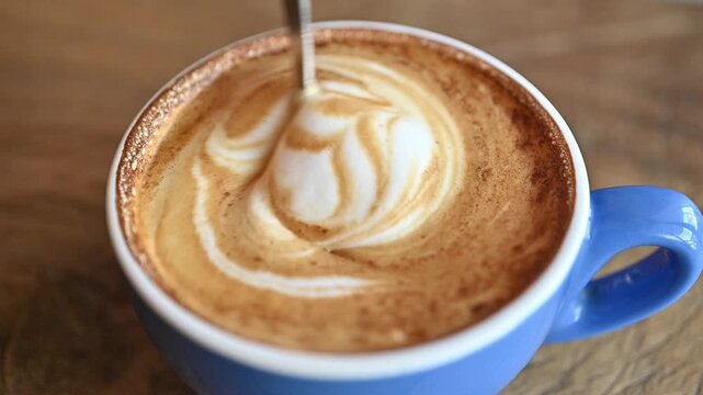High angle view of someone using spoon for stirring hot latte coffee before drinking.