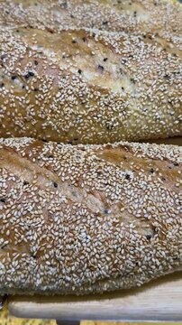 Close-up vertical video of golden sesame baguette with crisp crust and scattered sesame seeds.
