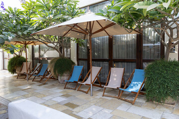 A tranquil outdoor lounge area featuring wooden sunbeds with umbrellas. The space is surrounded by lush greenery, offering a peaceful environment perfect for relaxation or leisure time