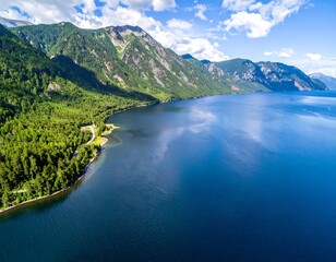 Aerial view of a deep blue lake framed by lush green forests and majestic mountain ranges