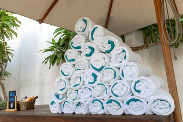 A neatly arranged stack of rolled white towels with turquoise trim placed on a wooden surface,...