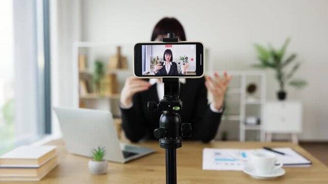Caucasian adult woman practicing meditation at work, recording session using smartphone and tripod.