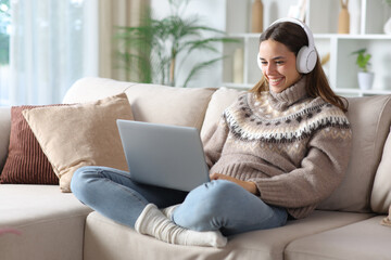 Happy woman in winter using laptop and headphone at home