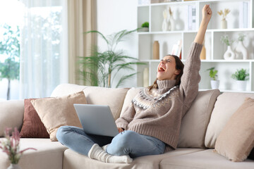 Excited woman celebrating success with a laptop in winter