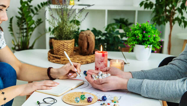 Numerology Divination consultation: woman writing in a notebook, man holding fortune stones.