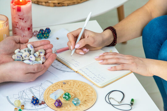 Numerology Divination consultation: woman writing in a notebook, man holding fortune stones.