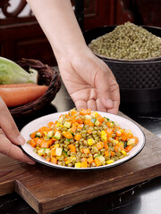 Hands Serving Colorful Fried Wheat Kernel Vegetable Salad on Wooden Board - Healthy Grain Dish
