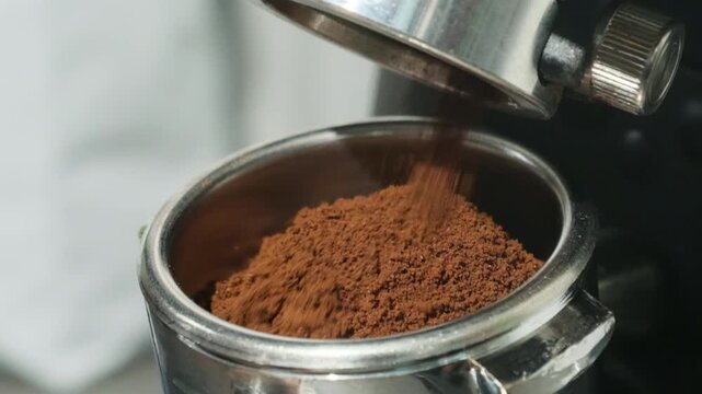 Professional barista transfers ground coffee into metal portafilter with espresso machine dispensing coffee powder in delicate stream slow motion