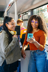 Diverse female friends discussing content on a smartphone while traveling on public transportation, enjoying their city commute