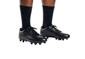 Black leather football cleats with aggressive tread pattern on feet in dark athletic socks, isolated on a transparent background