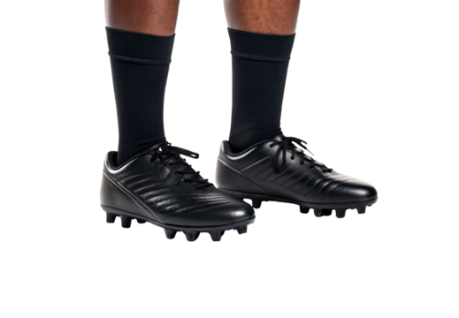 Black leather football cleats with aggressive tread pattern on feet in dark athletic socks, isolated on a transparent background