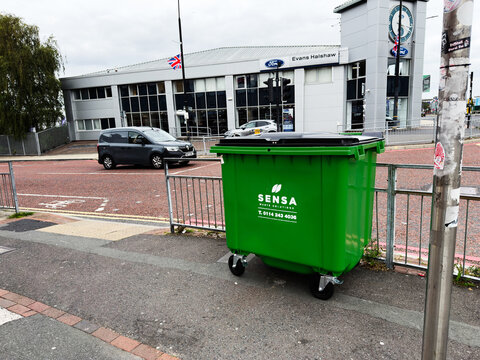 Green waste bin on city street in Manchester UK near Ford dealership and clock tower