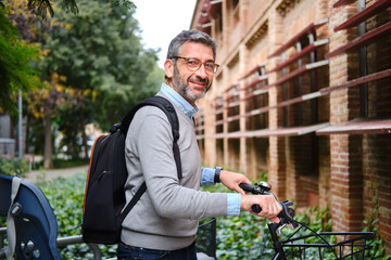 Mature man with glasses pushing bicycle on city street looking at camera