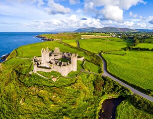 Aerial view showcases a historic stone fortress overlooking the coast. Rolling hills meet the ocean