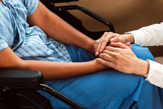 Close-up of a caregiver gently holding a patient's hands in a wheelchair, conveying comfort and support in a healthcare setting.