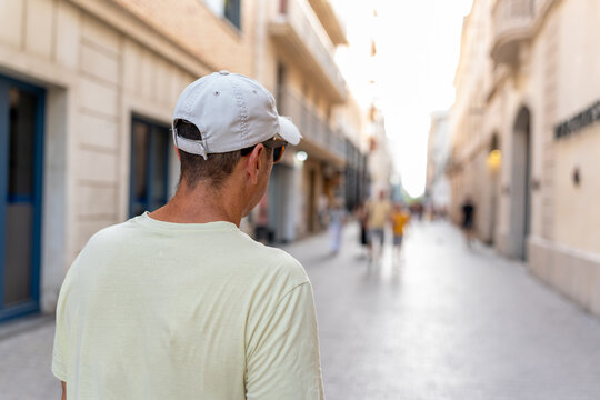 Man traveling, wearing cap and t-shirt, walking down a city street on vacation