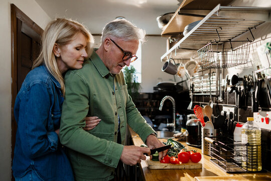 Senior couple cooking together in the kitchen, embracing and preparing vegetables for a healthy meal - Powered by Adobe