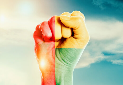 Guinea-Bissau national flag fist raise in the sky. The hand with flag raise in beautiful soft sky. Guinea-Bissau national flag for independence day.