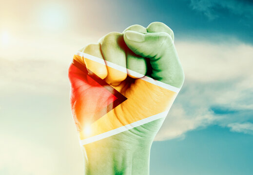 Guyana national flag fist raise in the sky. The hand with flag raise in beautiful soft sky. Guyana national flag for independence day.