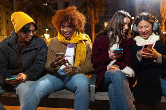 Diverse young friends using phones laughing at night