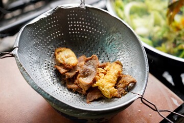 Fried pork draining in a metal strainer at a street food kitchen
