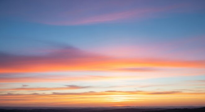 A vibrant sunset with a colorful sky and clouds, featuring a mix of warm and cool tones, with a mountain range in the background.