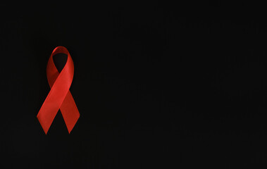 Closeup red ribbon symbolize HIV, world AIDS day awareness ribbon on black background, healthcare and medicine concept.