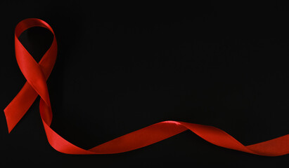 Closeup red ribbon symbolize HIV, world AIDS day awareness ribbon on black background, healthcare and medicine concept.