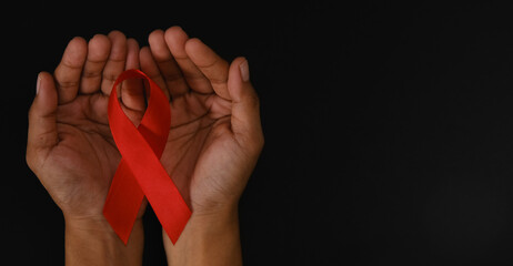 Hands holding red ribbon on black background, hiv awareness concept, world AIDS day, world hypertension day, world cancer day