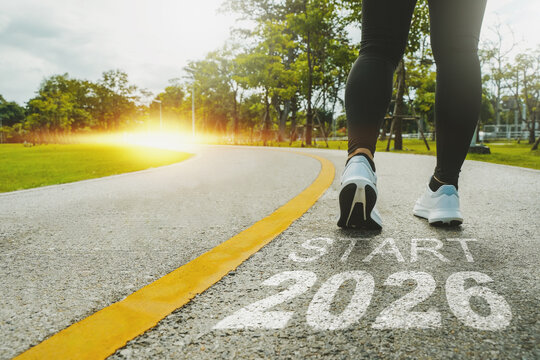 New Year 2026 concept. The beginning of success. The text 2026 is written on a paved road and a female runner is starting a new year. Concept of challenges or career paths and changes coming year.