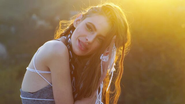 The woman portrait glows in golden light. Girls hair shines in the sunset. Woman looks dreamy and intense. The wind moves hair softly. Sunlight on beauty female face. Dreamy look of boho style girl.