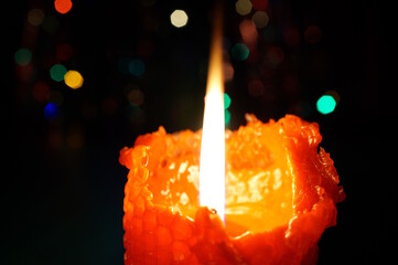 A burning red candle on a dark background.