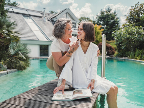 Mother and daughter studying together at poolside near house in summer