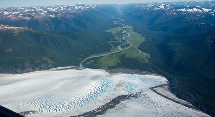 Aerial vista of a glacier flowing into a verdant valley, surrounded by snow-capped mountains